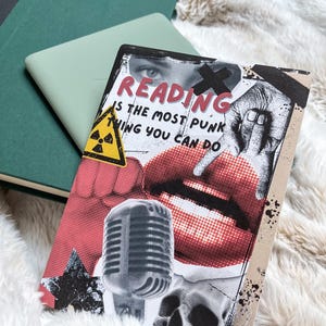 May include: A book cover with the text "READING is the most punk thing you can do" featuring a microphone, skull, and red lips. The cover is on a fluffy white surface with green books in the background.