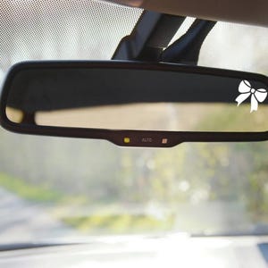 May include: A rearview mirror with a white bow sticker on the glass. The mirror has an "AUTO" button.