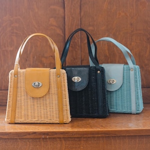 May include: Three woven straw handbags with leather accents. The handbags are in natural, black, and light blue.