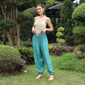 May include: A woman wearing a white crochet top and teal blue printed harem pants. The pants have an elastic waistband and a loose, flowing fit.