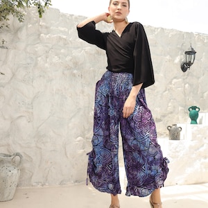 May include: A woman is wearing a black wrap top with a long sleeve and a pair of purple and blue patterned pants with a wide leg and a ruffled hem.