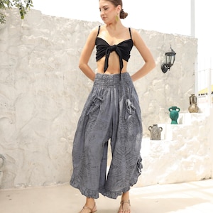 May include: A woman wearing a black crop top with a bow and gray printed wide-leg pants with a ruffled hem.