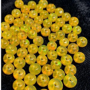 May include: A collection of yellow-orange gemstone beads with a hole drilled through the center. The beads have a translucent quality, with hints of green and orange visible within. The beads are round and appear to be polished.