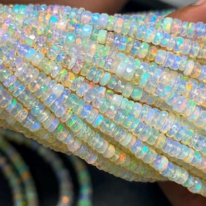 May include: A strand of small, faceted, round opal beads featuring a translucent white base with vibrant, multi-colored iridescent flashes of green, blue, yellow, and orange throughout each individual bead, arranged in a dense, uniform row.