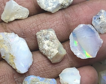 May include: A selection of raw opal gemstones, showcasing a variety of shapes and sizes. The opals exhibit a spectrum of colours, including white, blue, and iridescent flashes. Some have a rough, textured surface, while others appear smoother.