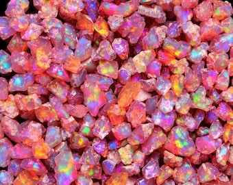 May include: A collection of small, raw, pink-toned opal gemstones featuring a vibrant play-of-colour with flashes of neon green, bright yellow, and electric blue throughout the irregular, faceted surfaces of each individual stone.
