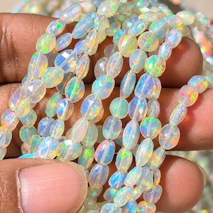 May include: A strand of faceted oval-shaped opal beads featuring a translucent white base with vibrant flashes of iridescent green, yellow, orange, and blue light reflecting from within each individual gemstone bead.
