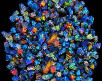 May include: A collection of small, raw, dark blue opal gemstones arranged in a circular cluster. Each individual stone displays a vibrant play of colour, featuring flashes of bright neon green, orange, and yellow against a deep blue base.