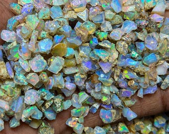 May include: A collection of small, raw opal gemstones featuring a translucent white base with vibrant flashes of iridescent blue, green, and pink light. These irregular, jagged mineral fragments display a natural, unpolished texture.