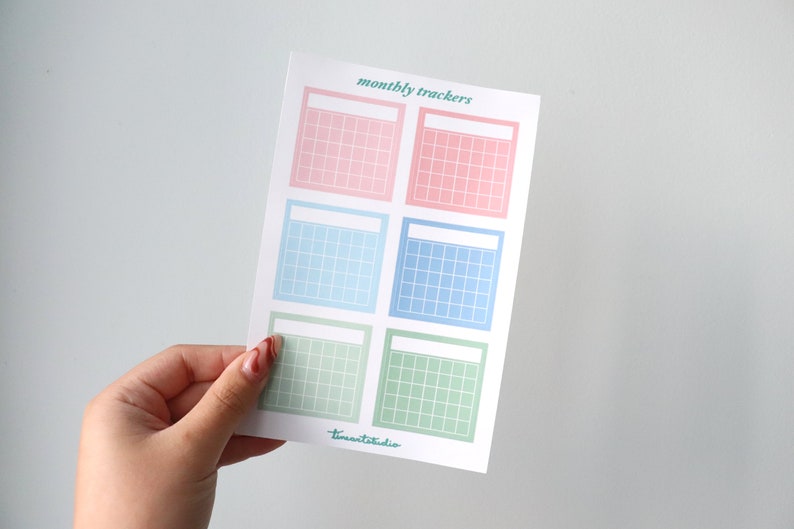Op de afbeelding: Een vel met zes printbare maandelijkse trackers in pastelroze, blauw en groen. Elke tracker heeft een lege ruimte bovenaan voor een titel en een raster van vierkanten om data te markeren.