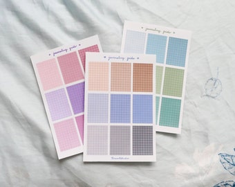 May include: Three sheets of gridded stickers in various pastel colors. Each sheet has nine squares with a grid pattern. The text "journaling grids" is printed on each sheet.