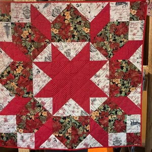 May include: A red and white quilt with a star pattern in the center. The quilt is made of various fabrics with floral and text designs. The quilt is perfect for a winter or holiday theme.