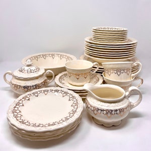 May include: A set of vintage white porcelain dinnerware with gold trim. The set includes plates, bowls, cups, saucers, a creamer, and a sugar bowl. The dishes feature a delicate floral pattern.