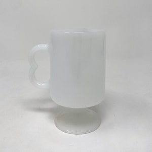 May include: White ceramic mug with a heart-shaped handle and a pedestal base.