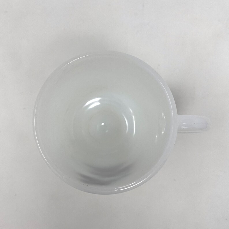 May include: White ceramic coffee mug with a rounded handle. The mug is empty and has a smooth, glossy finish.