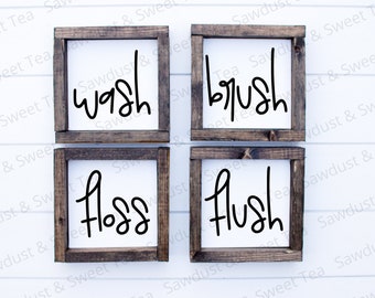 May include: Four wooden signs with the words "wash", "brush", "floss", and "flush" written in black cursive font. The signs are arranged in a square shape on a white background.