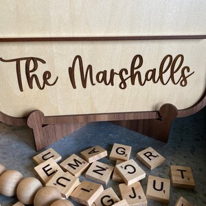 May include: A wooden sign with the text "The Marshalls" engraved on it. The sign is sitting on a wooden stand and there are wooden letter tiles scattered around it.