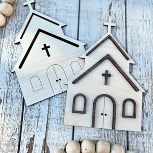 May include: Two unfinished wooden church cutouts with a brown stain around the edges. The cutouts have a cross on the front and windows on the sides.