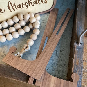 May include: A wooden sign with the text "The Marshalls" engraved in it. The sign is propped up on a wooden stand.