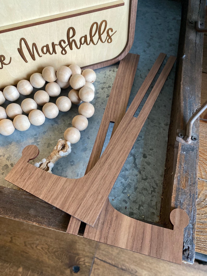May include: A wooden sign with the text "The Marshalls" engraved in it. The sign is propped up on a wooden stand.