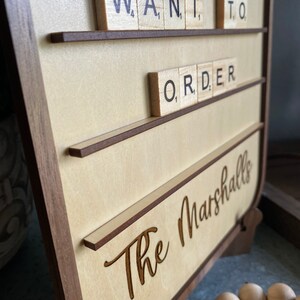 May include: A wooden sign with the words "Want to Order" spelled out in black tiles on a light wood background. The sign also has the words "The Marshalls" engraved in the wood.
