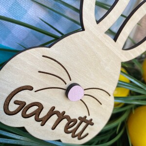 Puede incluir: Decoraci&oacute;n de Pascua de conejo de madera con una nariz rosa y el nombre "Garrett" grabado en ella.