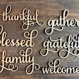 May include: A set of six wooden signs with cursive lettering. The words on the signs are "thankful", "gather", "blessed", "grateful", "family", and "welcome".