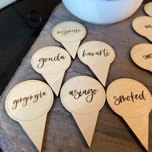 May include: Wooden cheese markers with the names "gorgonzola", "smoked", "asiago", "havarti", "gouda", "mozzarella", "brie", and "swiss" written on them.