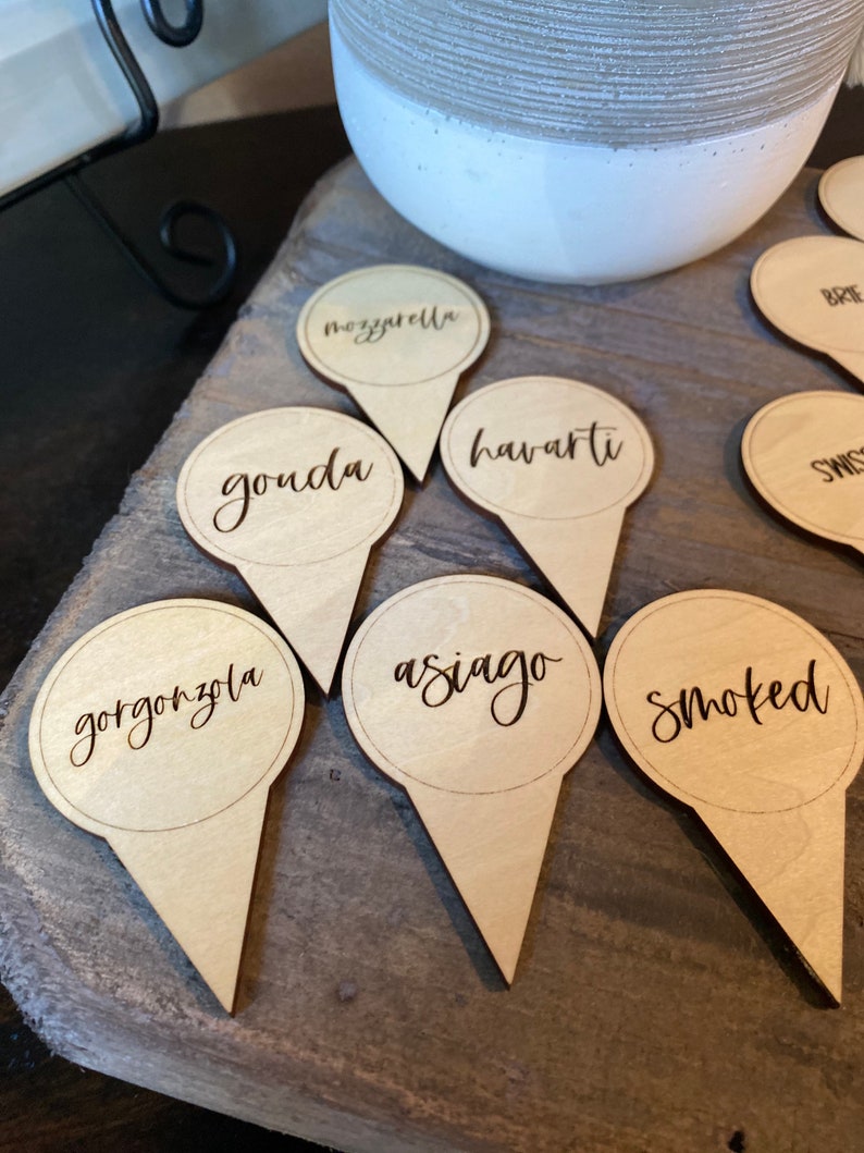 May include: Wooden cheese markers with the names "gorgonzola", "smoked", "asiago", "havarti", "gouda", "mozzarella", "brie", and "swiss" written on them.