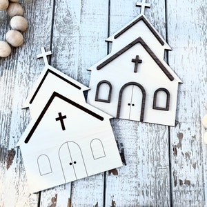 May include: Two unfinished wooden church cutouts with a brown outline. The church cutouts have a cross on the top and windows and a door on the front.