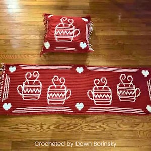 May include: A red crocheted pillow and table runner set. The pillow and runner feature white crocheted designs of coffee cups and hearts. The table runner has a fringed edge and is decorated with four coffee cup designs.