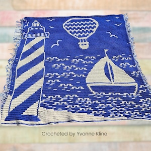 May include: A blue and white crocheted blanket with a lighthouse, sailboat, and hot air balloon design. The blanket has a fringed edge and the text "Crocheted by Yvonne Kline" is at the bottom.