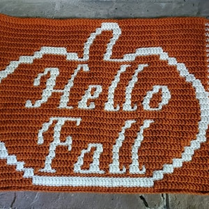 May include: A crocheted doormat with a pumpkin shape and the words "Hello Fall" in white yarn on an orange background.