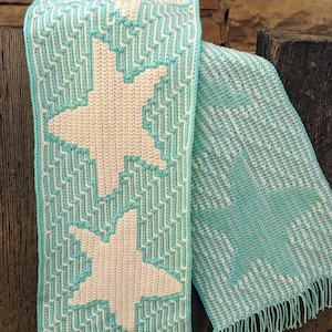 May include: A crocheted scarf with a white star pattern on a turquoise background. The scarf has fringe on both ends.
