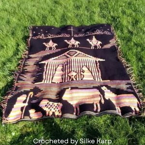 May include: A black and tan crocheted blanket featuring a nativity scene with camels, a stable, and animals. The blanket has a fringed edge and the text "Crocheted by Silke Karp" at the bottom.