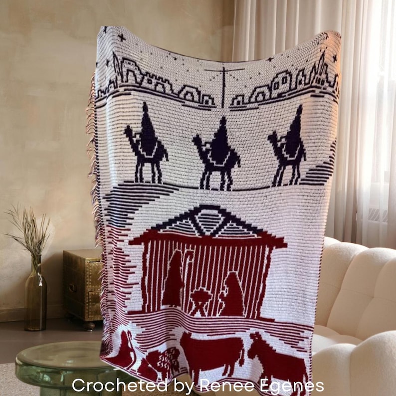 May include: A white and burgundy crocheted blanket featuring a nativity scene with camels, a stable, and animals. The blanket has a fringed edge and the text "Crocheted by Renee Egenes" at the bottom.