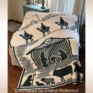 May include: A cream-colored crocheted blanket with a black nativity scene design. The blanket features images of the three wise men, a stable, and other biblical figures. The text "Crocheted by Cheryl Ridenour" is at the bottom.