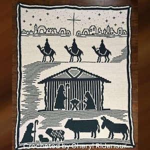 May include: Cream-colored crocheted blanket with a dark green nativity scene design. The blanket features silhouettes of the three wise men on camels, a stable, and various animals. The text "Crocheted by Cheryl Ridenour" is at the bottom.