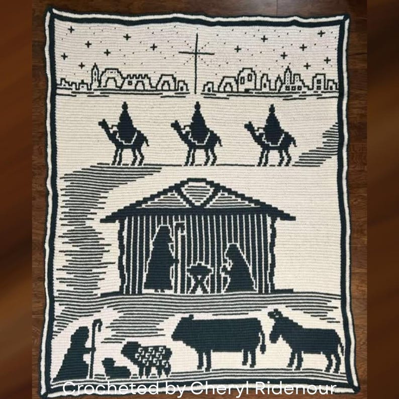 May include: Cream-colored crocheted blanket with a dark green nativity scene design. The blanket features silhouettes of the three wise men on camels, a stable, and various animals. The text "Crocheted by Cheryl Ridenour" is at the bottom.