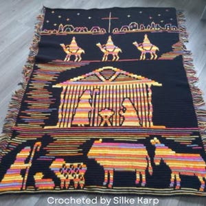 May include: Black crocheted blanket featuring a nativity scene with camels, a stable, and various animals. The blanket has a fringed edge and the text "Crocheted by Silke Karp" at the bottom.