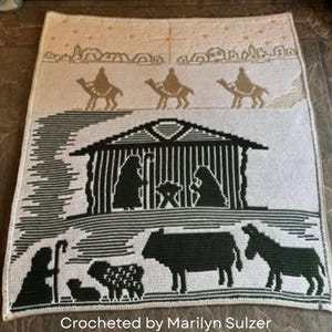 May include: A crocheted blanket featuring a nativity scene. The design includes silhouettes of the Holy Family, animals, and the Three Wise Men on camels. The text "Crocheted by Marilyn Sulzer" is at the bottom.