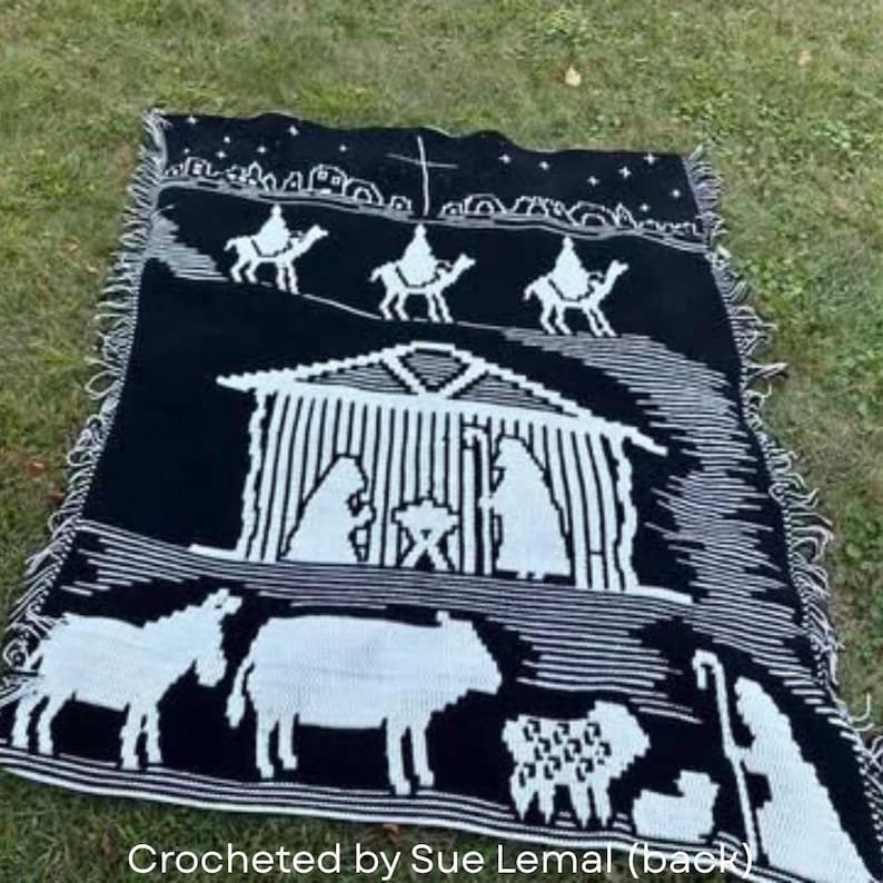 May include: Black and white crocheted blanket featuring a nativity scene. The blanket depicts the three wise men on camels, a stable with Mary, Joseph, and baby Jesus, and various animals. The text "Crocheted by Sue Lemal (back)" is visible.