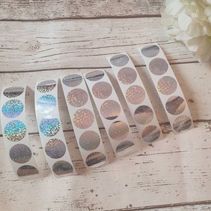 May include: Six vertical strips of circular adhesive stickers featuring a holographic finish that reflects light in various colours. Each strip contains multiple round stickers arranged in a single column on a white backing paper.