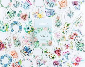 Peut inclure: Un ensemble d'autocollants floraux de différentes formes et tailles. Les autocollants présentent des illustrations à l'aquarelle de fleurs, de succulentes et de terrariums géométriques dans des tons de rose, de bleu et de vert. Une petite boîte d'autocollants est également visible, avec du texte en langue étrangère.