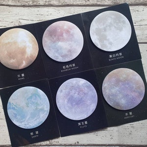 May include: A set of six circular sticky notes featuring celestial body illustrations on black square backings. The labels include Mars, Rainbow Moon, Black Moon, Earth, Pluto, and Mercury, each with corresponding Chinese and English text printed below.