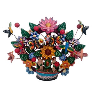 Puede incluir: Una escultura de cerámica colorida de árbol de la vida con un girasol, mariposas, pájaros y una pareja de pie frente a una serpiente. El árbol está en una maceta con detalles azules y verdes.