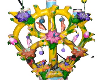 Puede incluir: Un árbol de cerámica amarillo con flores, pájaros y cuentas de colores. El árbol tiene una base redonda y está decorado con un patrón verde, amarillo y azul.