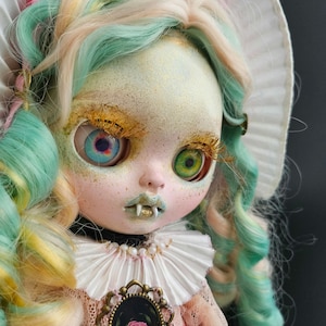 Könnte beinhalten: Eine Puppe mit langen, grünen und gelben Haaren, die einen weißen Spitzenkragen und ein rosa Kleid trägt. Die Puppe hat große, bunte Augen und ein aufgemaltes Lächeln.