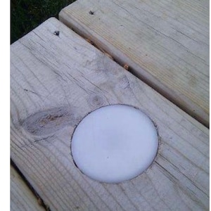 May include: A close-up of a wooden surface with a circular cutout. The cutout is filled with a white, round object.