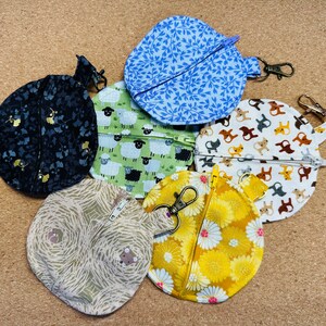 May include: Five different fabric coin purses with zipper closures. The purses are decorated with various patterns, including floral, animal, and geometric designs. The purses are in shades of blue, yellow, black, white, and green.